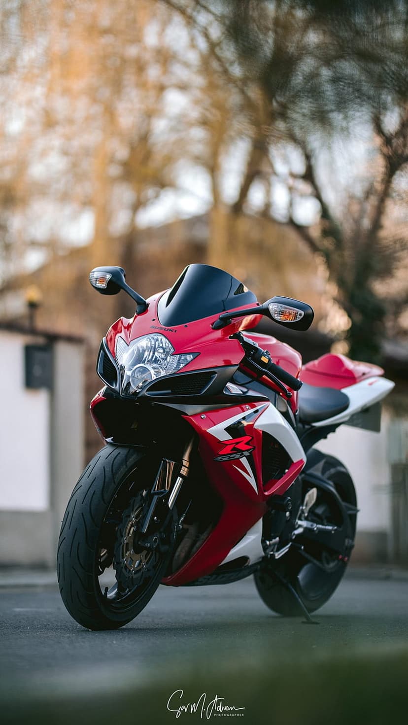 Suzuki GSXR sportbike with red and white fairings parked outdoors against a blurred background of green trees.