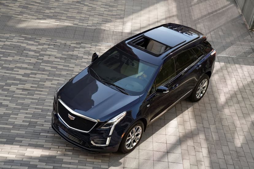 Dark blue Cadillac SUV from a high angle on a grey stone tiled plaza with an open sunroof and beige interior.