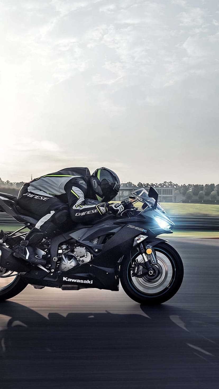 Kawasaki motorcycle racer wearing a Dainese suit leans into a track curve with motion blur and a bright sky.