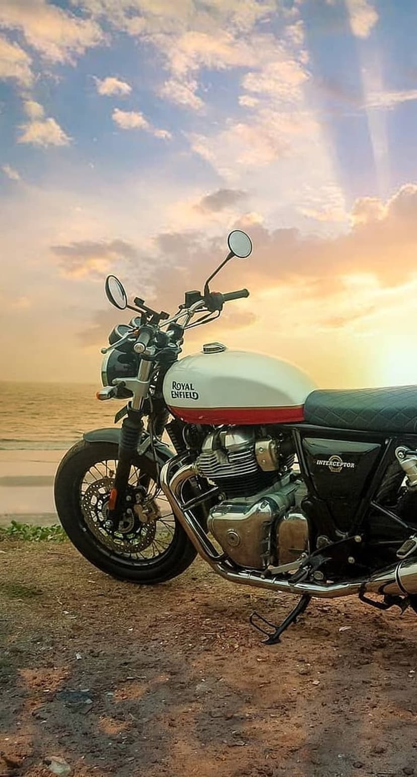 Royal Enfield Interceptor 650 motorcycle parked on a sandy beach during a vibrant orange and purple sunset.