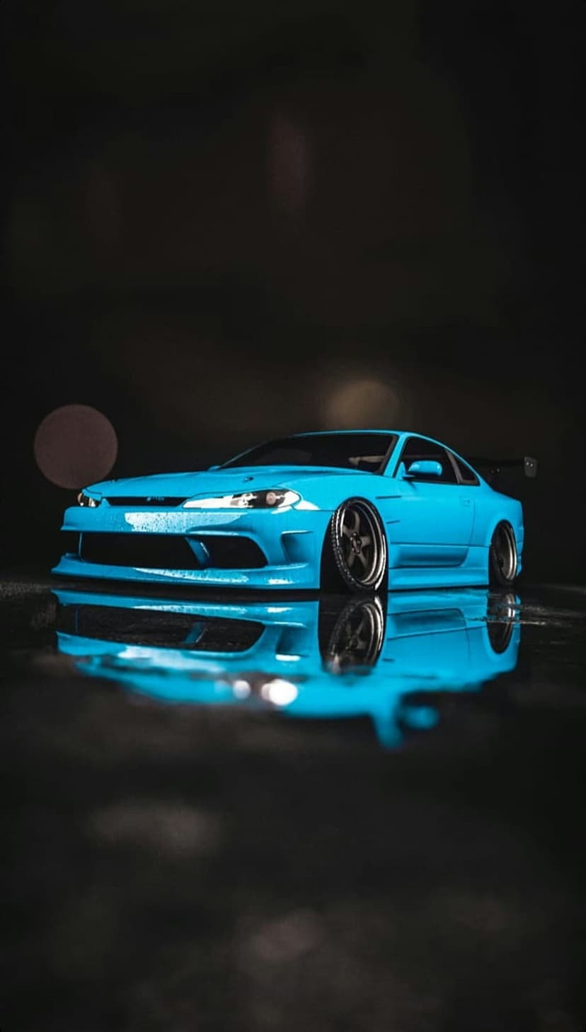 Blue modified sports car with a large rear spoiler parked on a wet, reflective surface with bokeh lights.