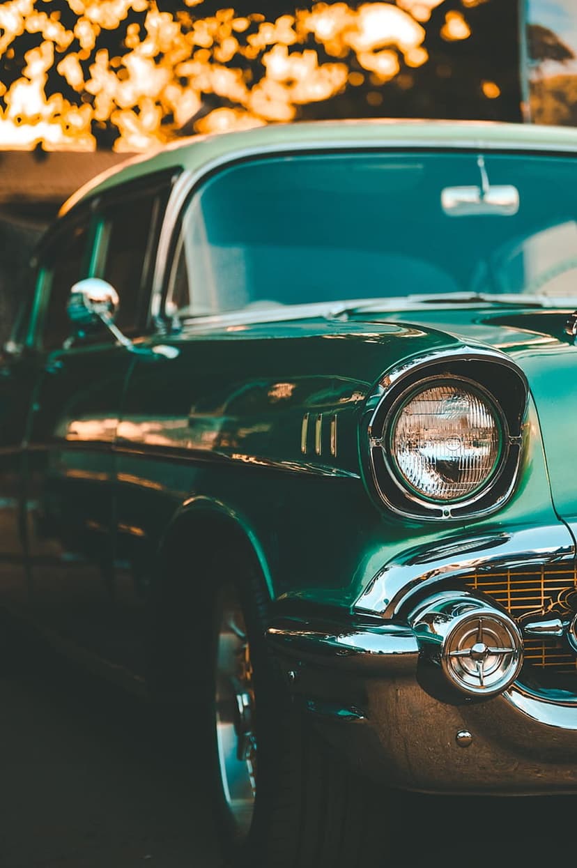 Mint green vintage Chevrolet Bel Air front headlight and chrome grille captured during a golden hour sunset.