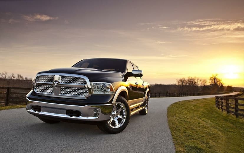 Black Ram 1500 pickup truck on a rural path at sunset with golden light reflecting off its chrome grille and rims.