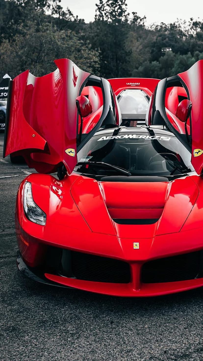 Red Ferrari with butterfly doors open upward on a dark asphalt road showing its aerodynamic body and interior.