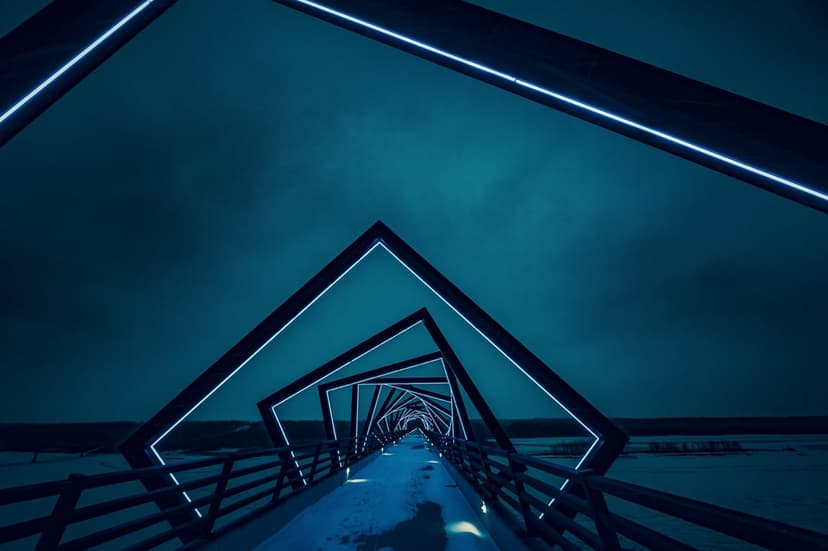 Blue neon geometric arches line a bridge at dusk, creating a glowing tunnel perspective toward the dark horizon.