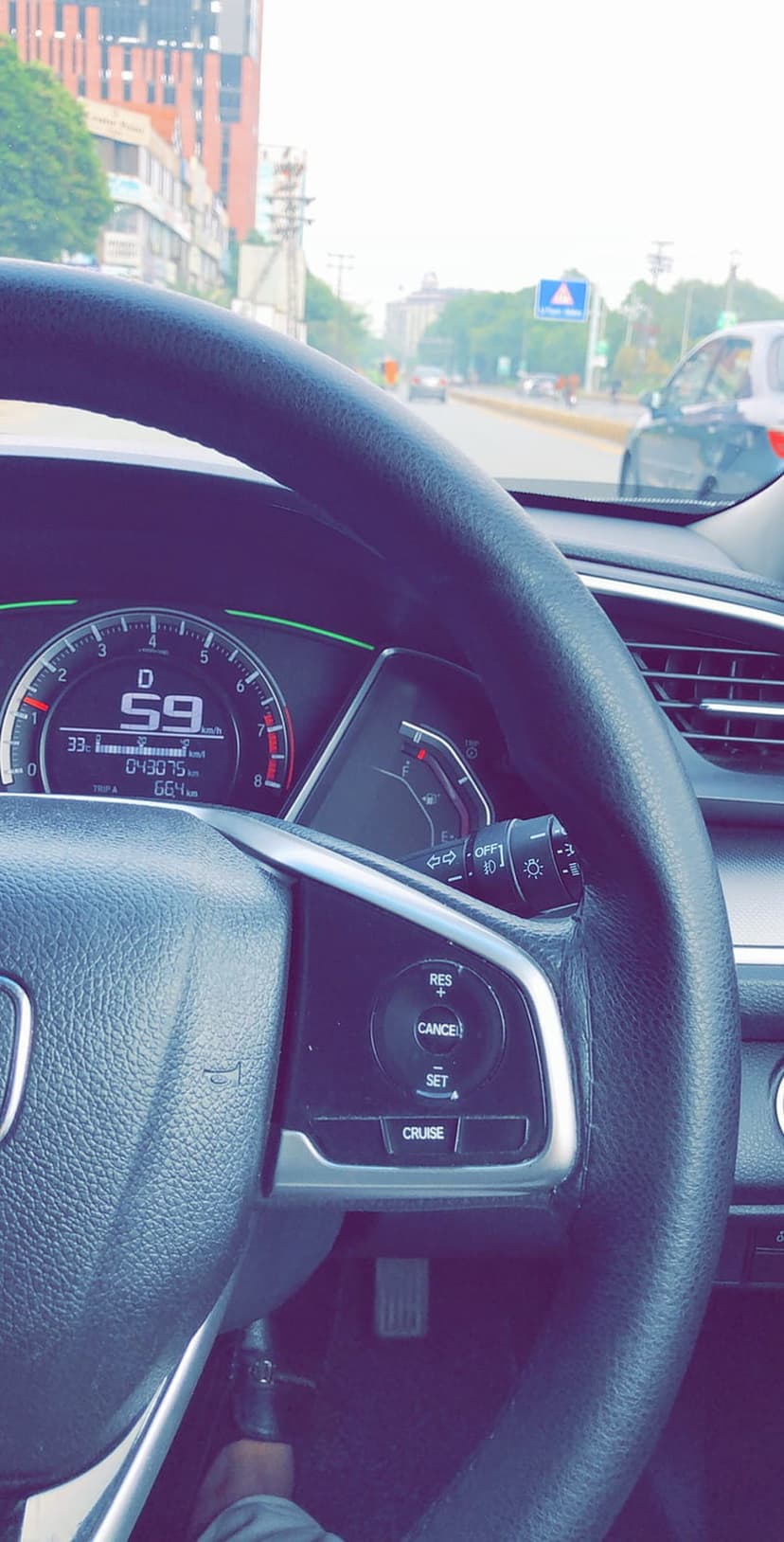 Digital car speedometer showing 59 km/h on a modern dashboard with a city street visible through the windshield.