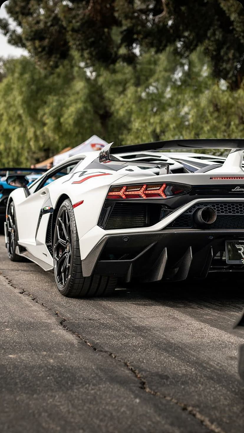 White Lamborghini Aventador SVJ rear view with a large spoiler and Y-shaped taillights on an asphalt road.