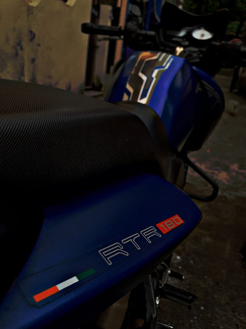 Blue TVS Apache RTR 180 motorcycle features a textured seat, RTR 180 badging, and a small Italian flag decal.