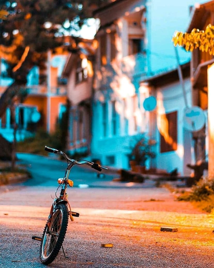 Vintage bicycle parked on an asphalt street with blurred blue and orange buildings in soft evening sunlight.