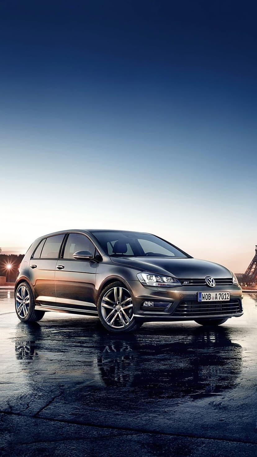 Dark gray Volkswagen Golf R parked on reflective wet asphalt under a blue twilight sky with low-angle framing.