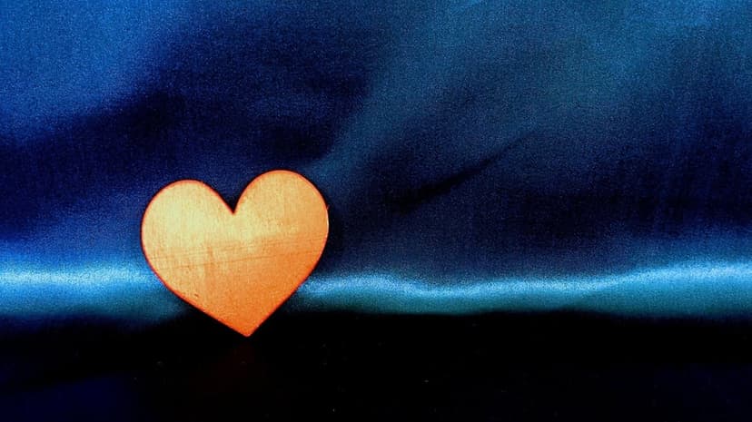 Solitary orange heart rests on pleated dark blue satin fabric with soft lighting and smooth textures.