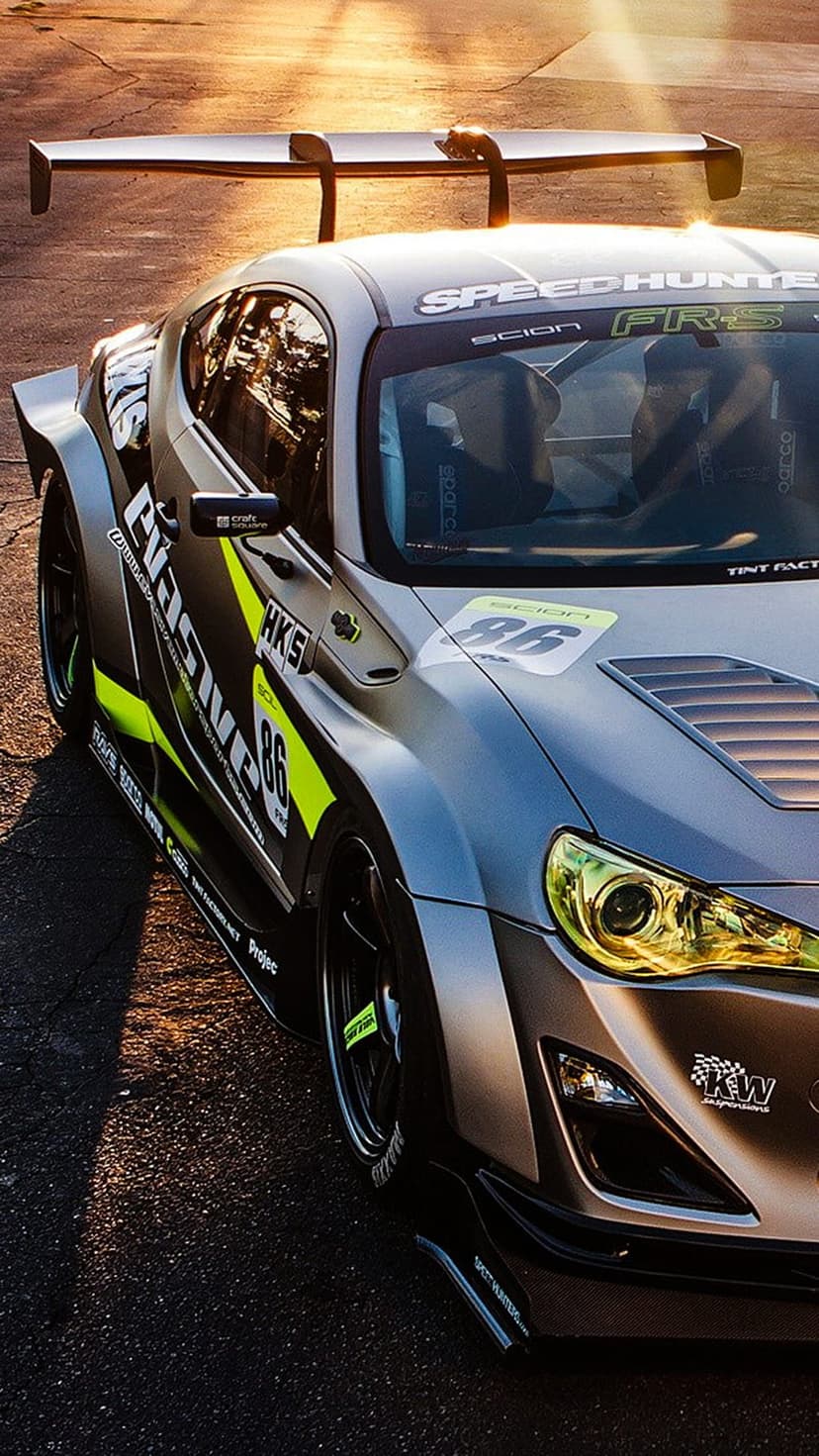 Scion FR-S with Speedhunters livery, large racing wing, and widebody kit parked on asphalt during golden hour.