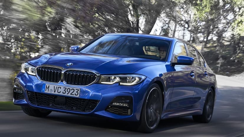 Blue BMW 3 Series sedan driving fast on a winding road with motion blurred trees in the background.