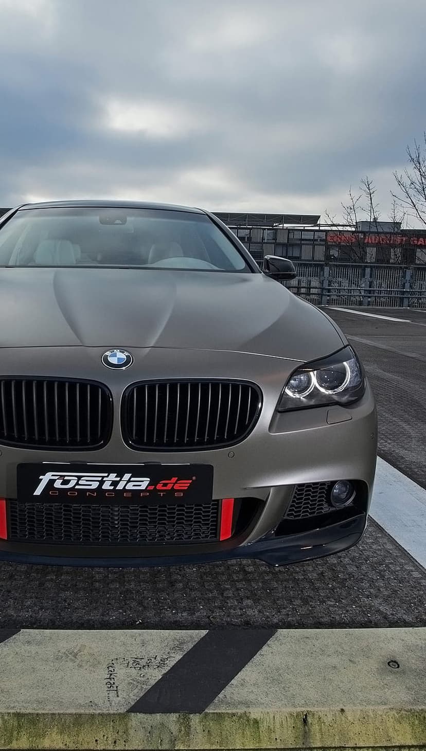 BMW F10 M Sport sedan front end with matte grey wrap, red bumper stripes, and custom grille graphics.
