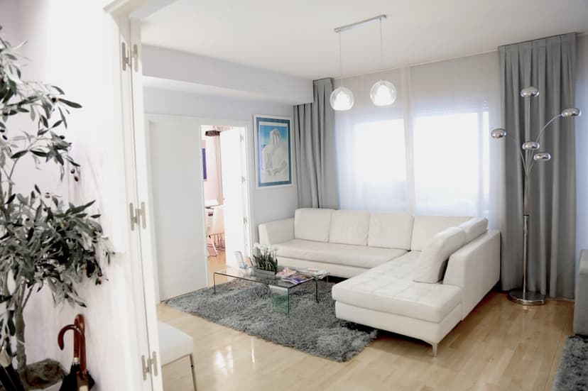 White sectional sofa on a gray shag rug next to a glass coffee table in a bright, modern minimalist living room.