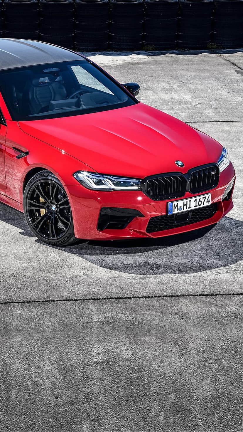 Red BMW M5 Competition sedan featuring sharp LED headlights and a black kidney grille on dark pavement.