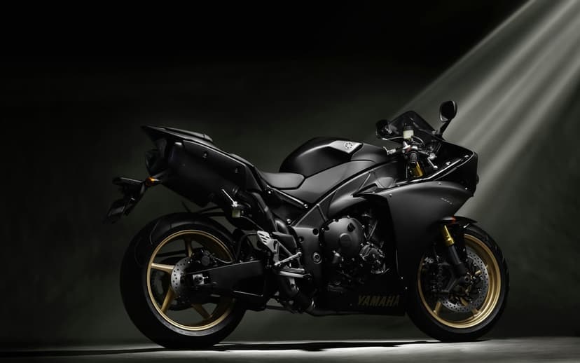 Matte black sportbike with gold wheels illuminated by dramatic light beams in a dark minimalist studio.