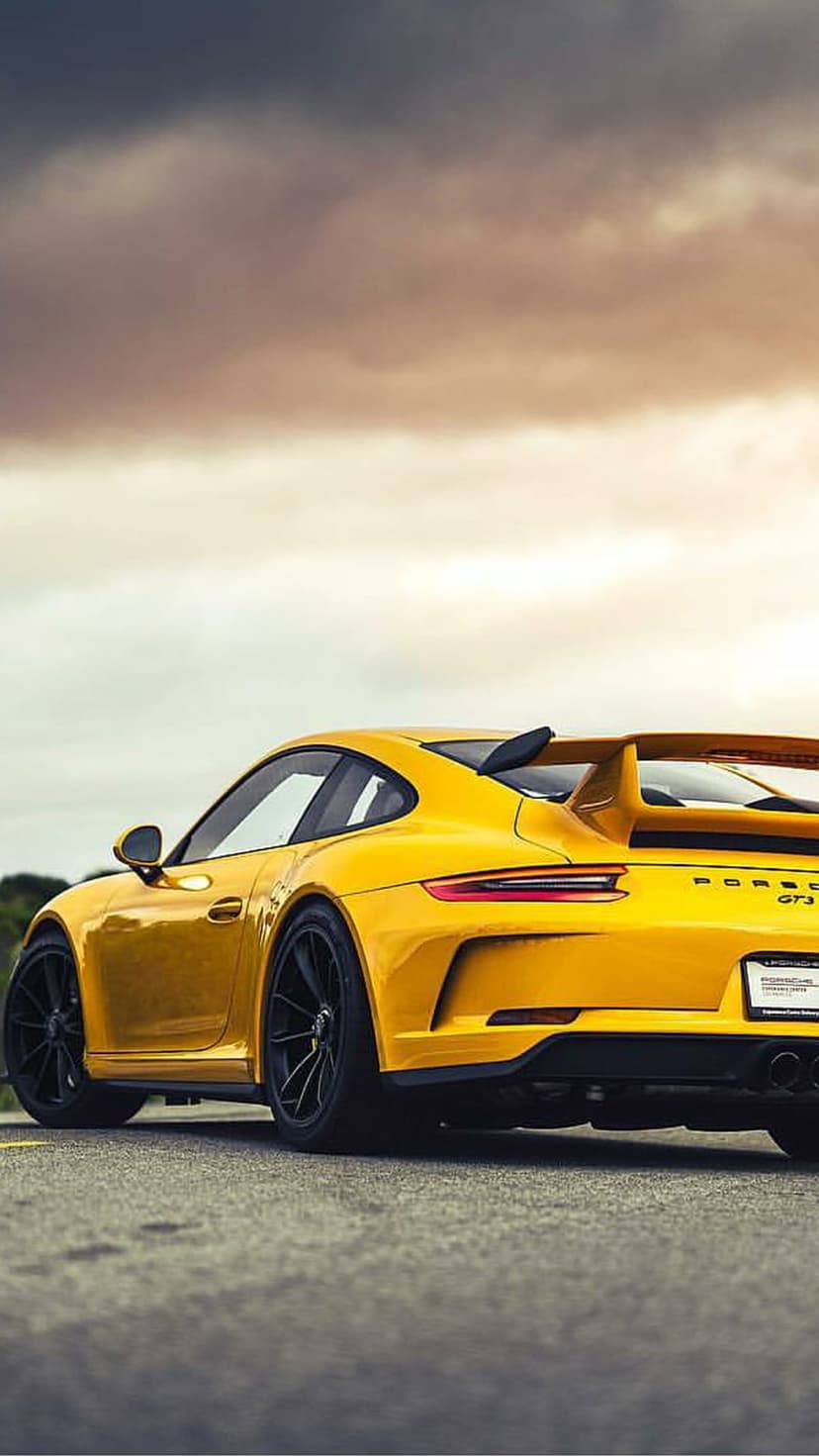 Yellow Porsche GT3 RS features a large rear wing and black rims against a dramatic, colorful storm cloud sky.