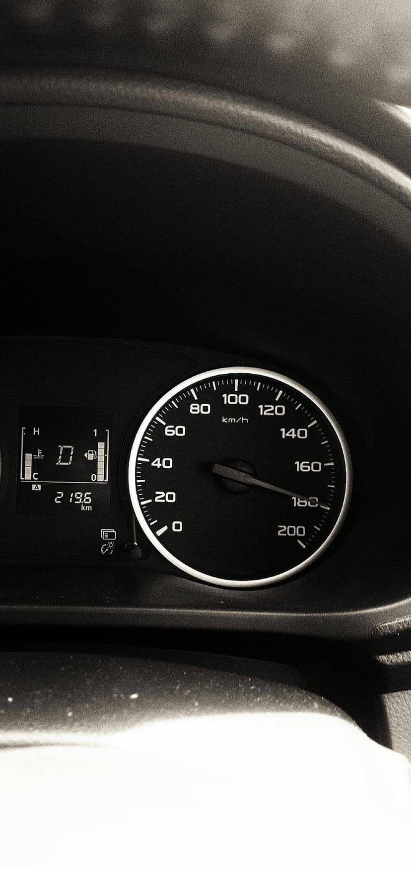 Black analog speedometer needle pointing at 120 km/h beside a digital display showing gear and fuel info.