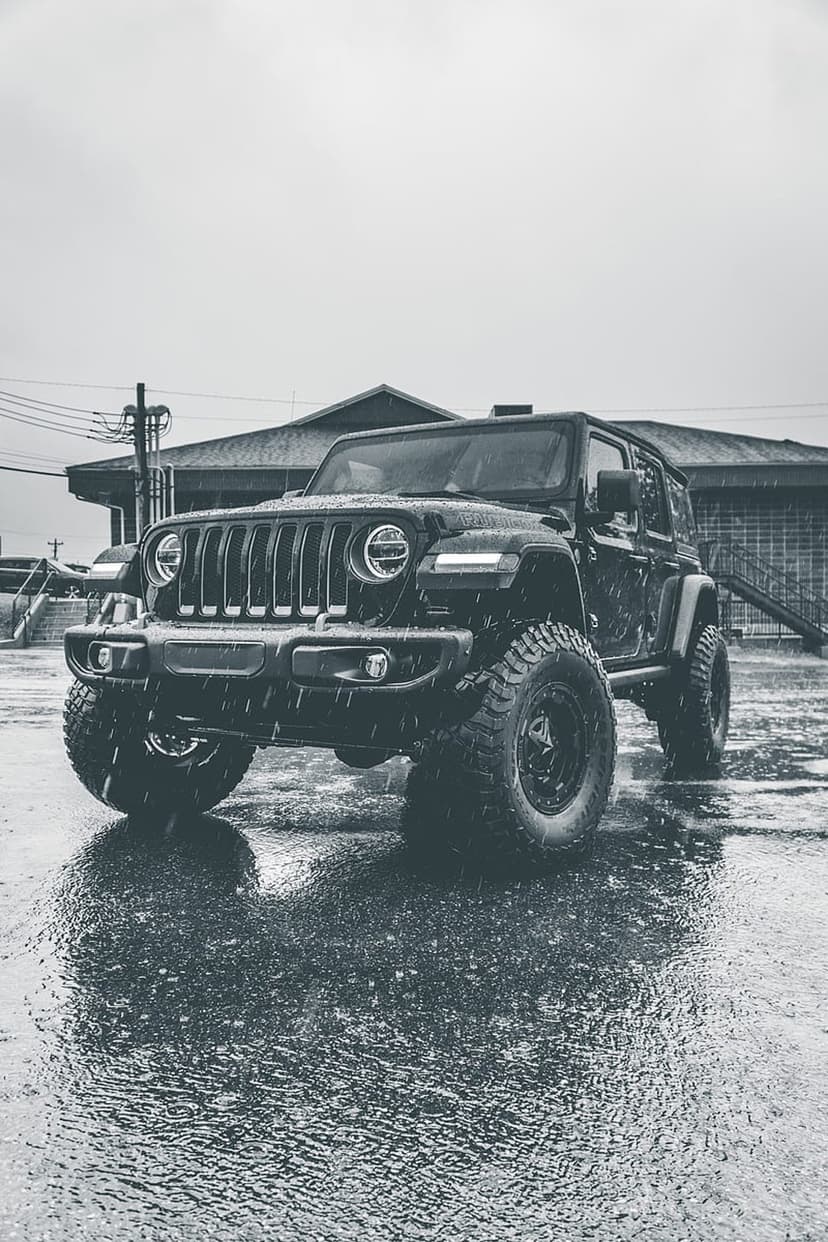 Jeep Wrangler on wet asphalt during rain with high-contrast monochrome tones and visible tire tread details.