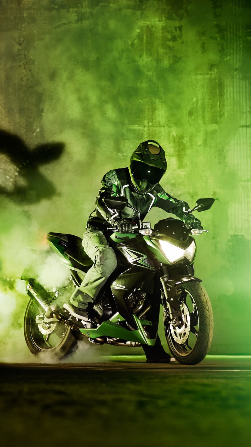 Motorcyclist in full gear performs a rear-wheel burnout surrounded by dense clouds of vibrant green smoke.