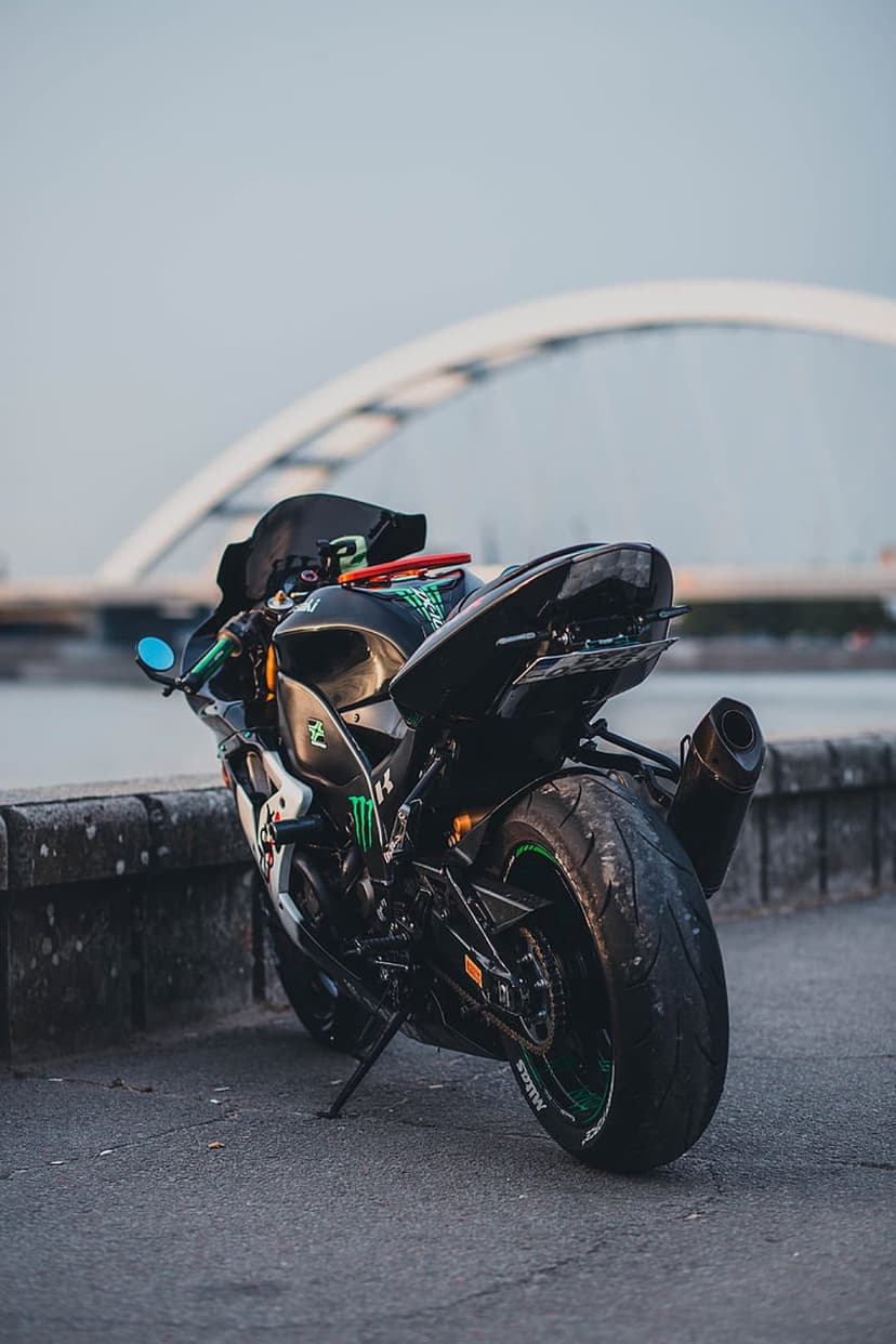 Black Kawasaki motorcycle with green accents parked near a white arched bridge during a hazy sunset.
