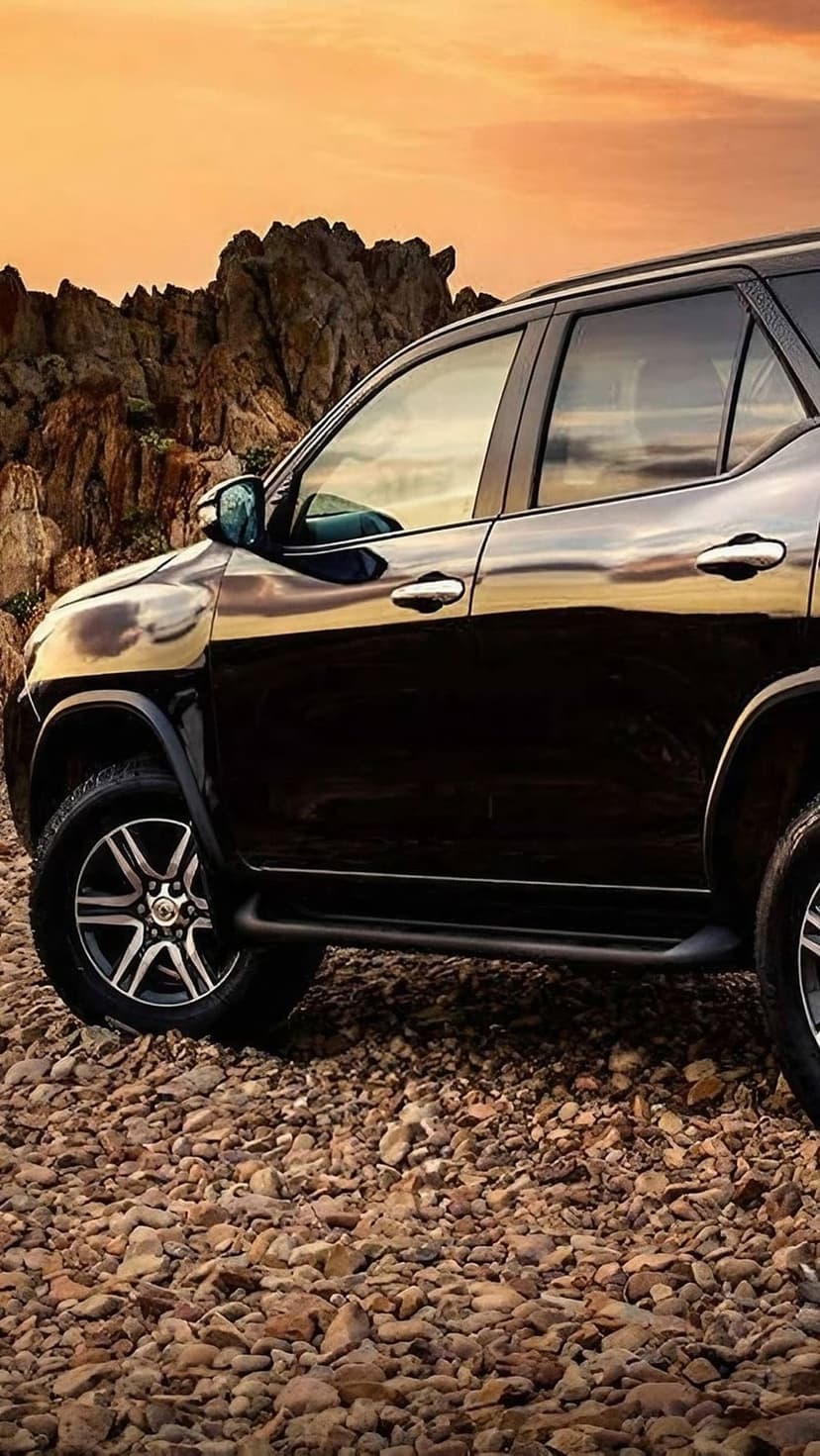 Black SUV parked on a jagged rock surface under a vibrant orange sunset sky with distant mountain peaks.