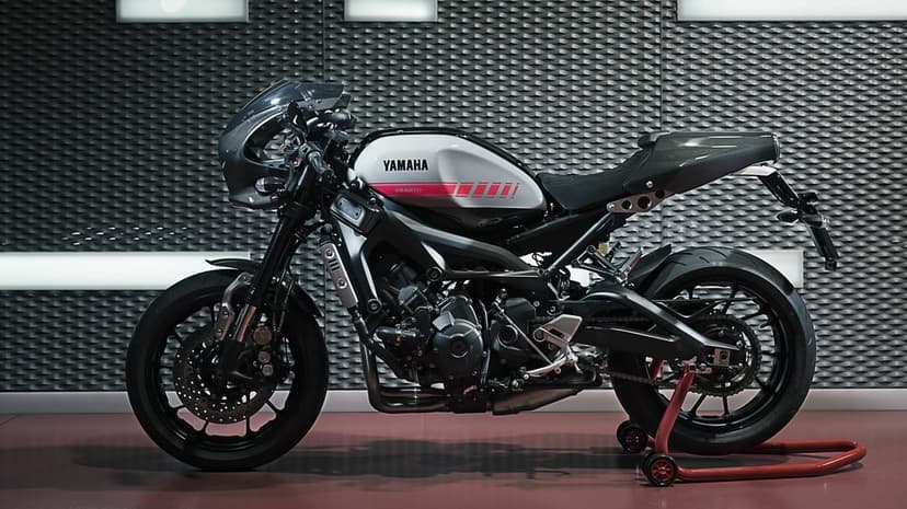 Side profile of a Yamaha XSR900 Abarth motorcycle against a textured industrial wall on a red paddock stand.