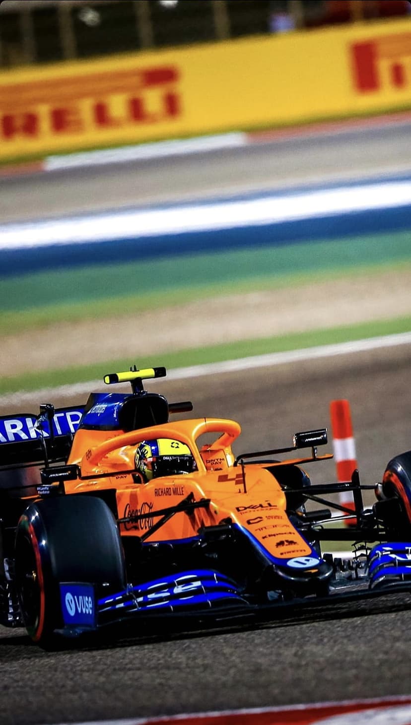 McLaren Formula 1 car in papaya orange and blue racing on a dark asphalt track under bright stadium floodlights.