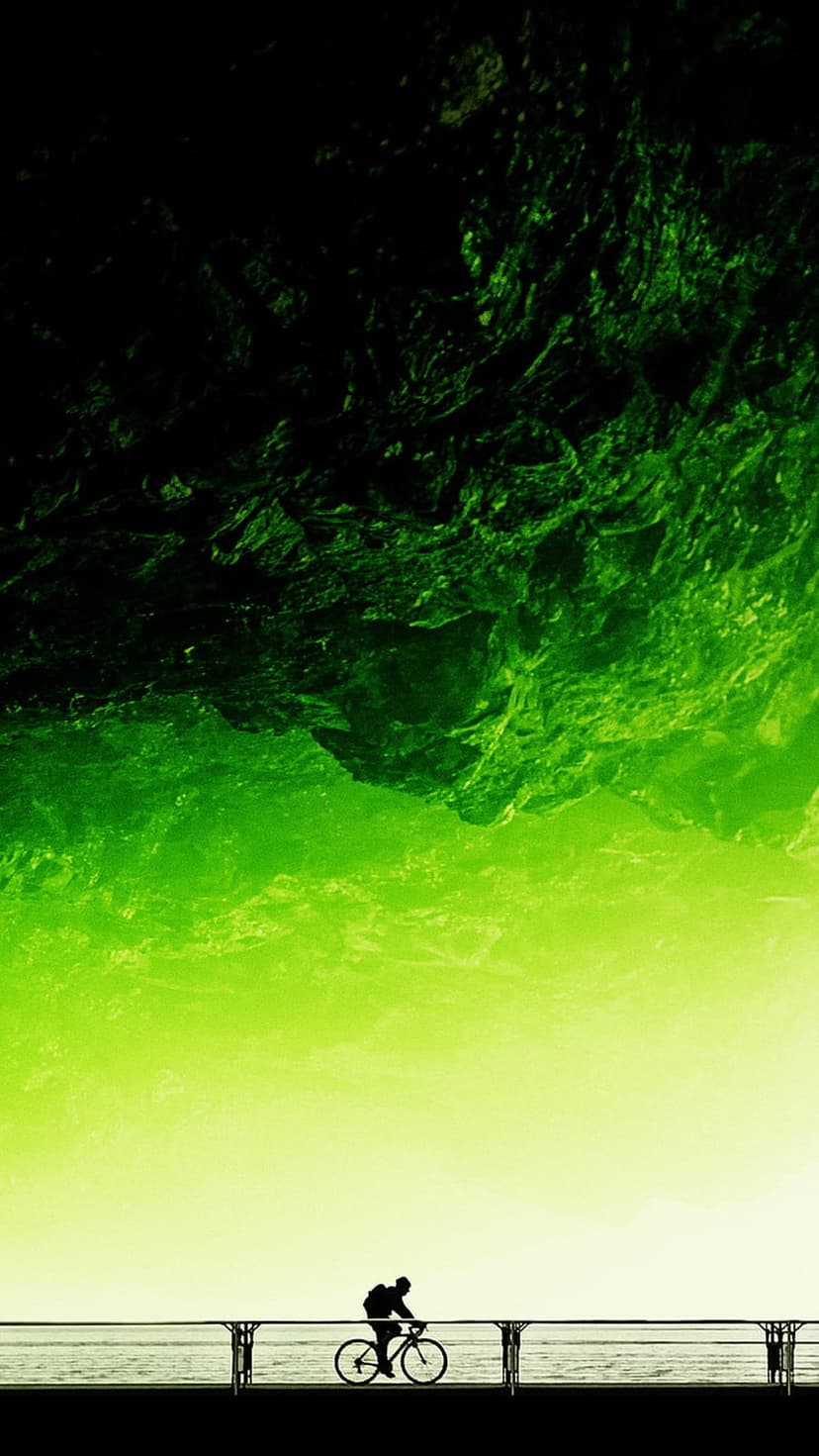Cyclist on a pier silhouetted against a lime green sky with dark rocky formations and a calm ocean view below.