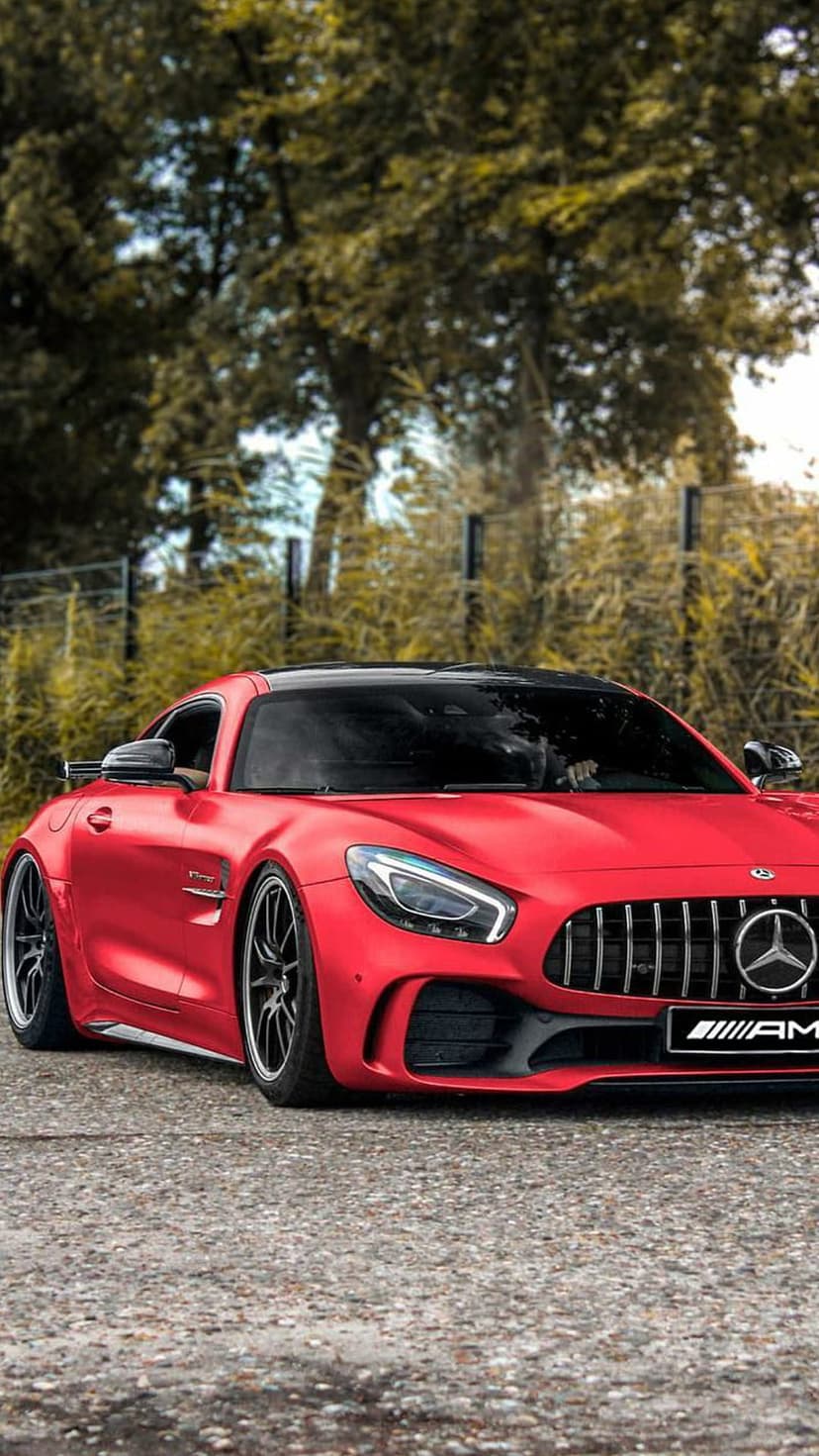 Red Mercedes-AMG GT S with black wheels parked on a gravel road against a lush forest backdrop in vertical view.