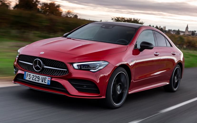 Red Mercedes-Benz luxury car driving on a rural road with motion blur and soft sunset lighting in the background.