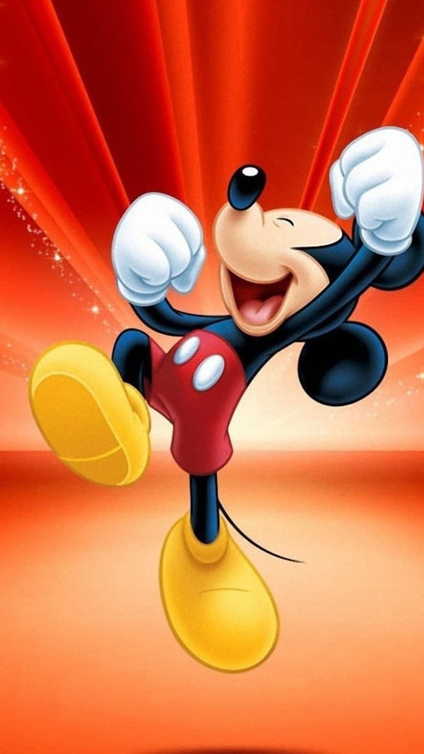 Mickey Mouse jumps with clenched fists and a wide grin amidst red and orange radiating lines and glowing sparkles.