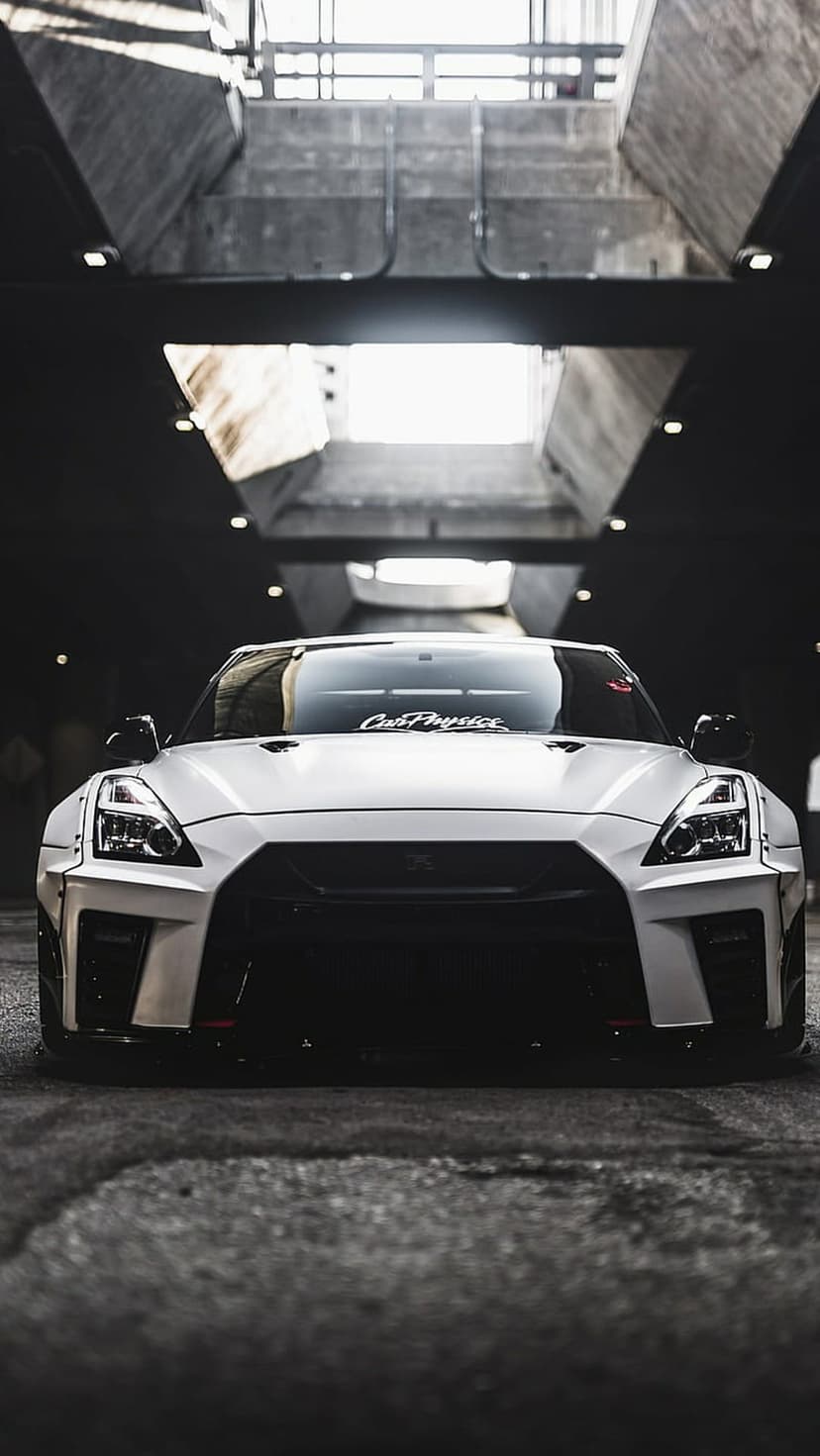 White Nissan GT-R sports car with a wide body kit parked in a dark concrete industrial garage under soft light.