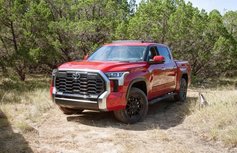 Red Toyota Tundra TRD pickup truck parked on a dirt path surrounded by green trees in bright daylight.