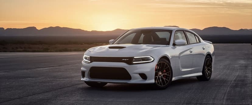 White Dodge Charger SRT Hellcat parked on an open runway with a golden sunset and mountains in the background.
