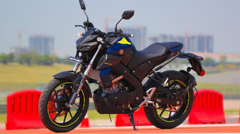 Yamaha MT-15 motorcycle with neon yellow accents parked on a track with a blurred urban city background.
