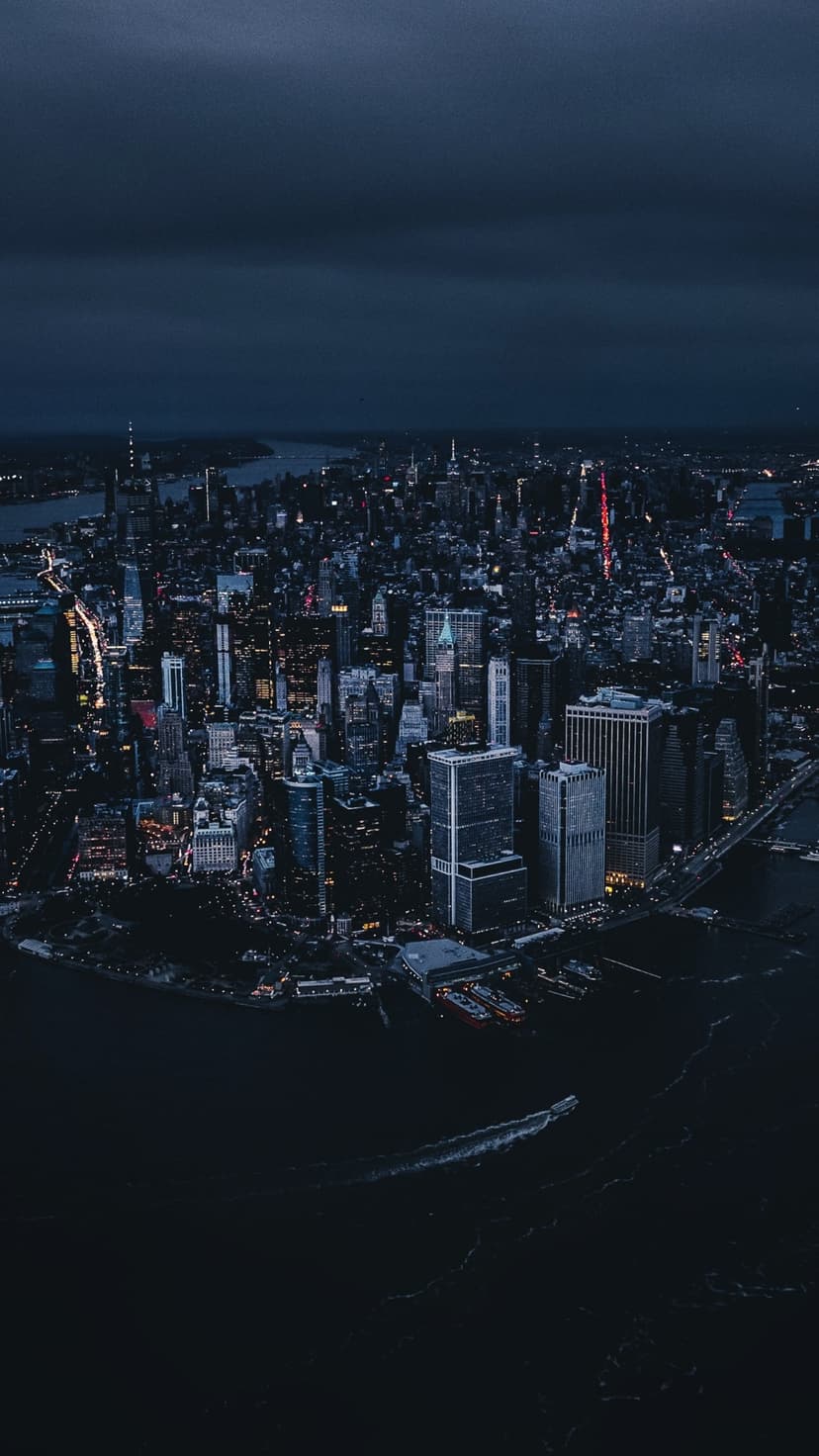 Illuminated New York City skyscrapers and dark river waters seen from above under a dramatic cloudy night sky.