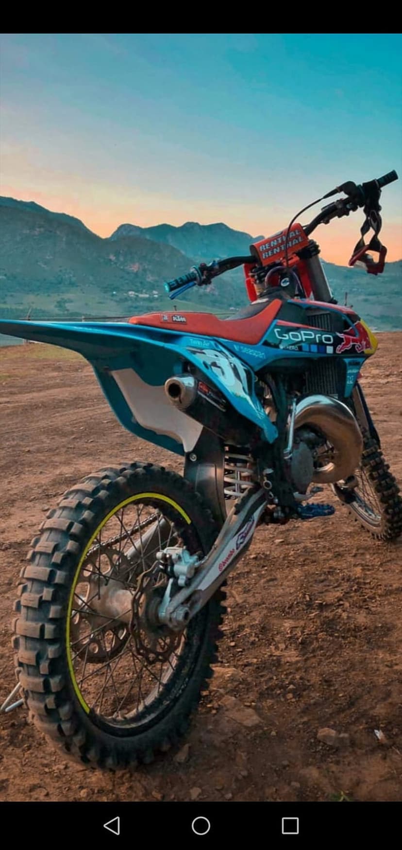 Dirt bike with knobby tires parked on a dusty trail against a sunset mountain range during golden hour.