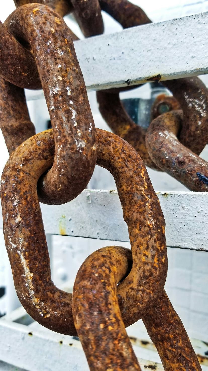 Rusty interlocking metal chain links with heavy orange oxidation and dark patina against a white background.