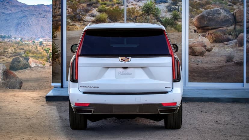 Rear view of a white Cadillac Escalade SUV parked in front of mirrored glass reflecting a desert landscape.