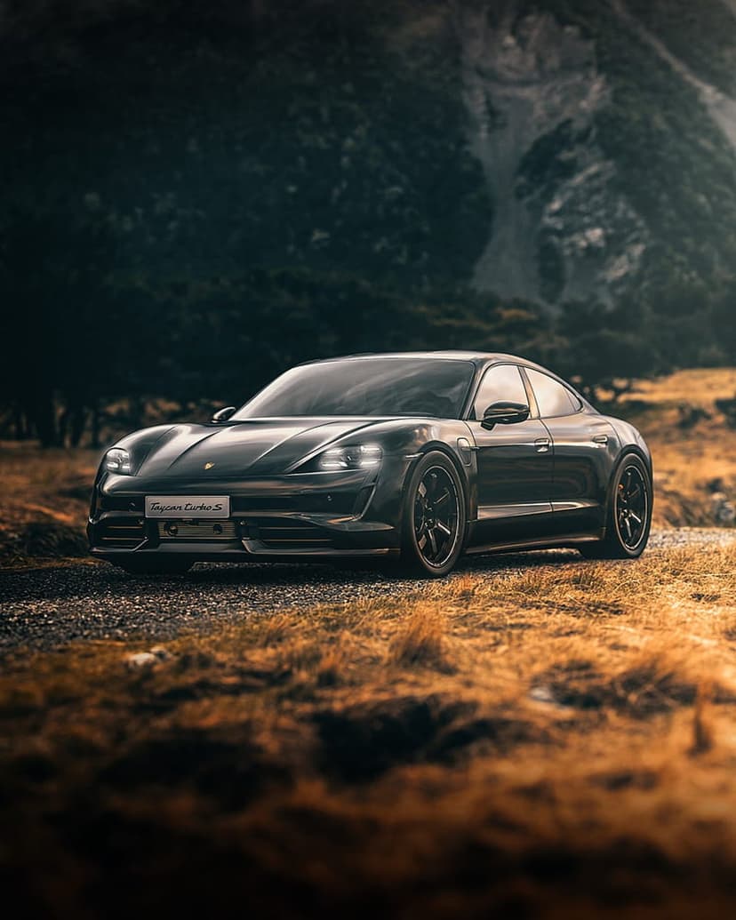 Black Porsche Taycan Turbo S drives on a path through golden grass with tall rocky mountains in the background.
