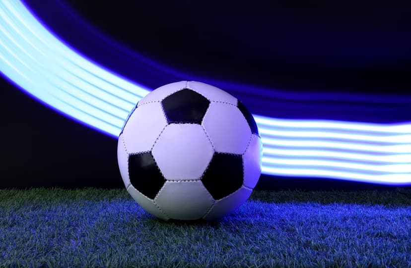 Soccer ball on green turf surrounded by glowing blue motion streaks and light trails in a dark setting.