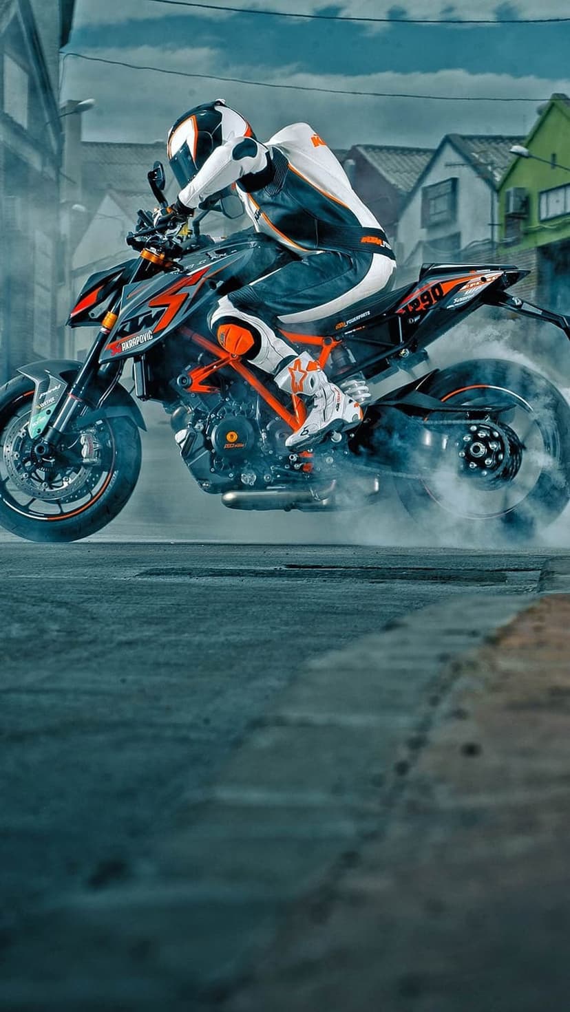 Motorcyclist in black gear performs a wheelie on an orange bike with thick white smoke on a blurred street.
