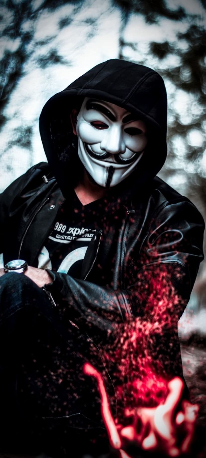 Anonymous masked figure in a leather jacket holds a hand radiating vibrant red light against a dark background.