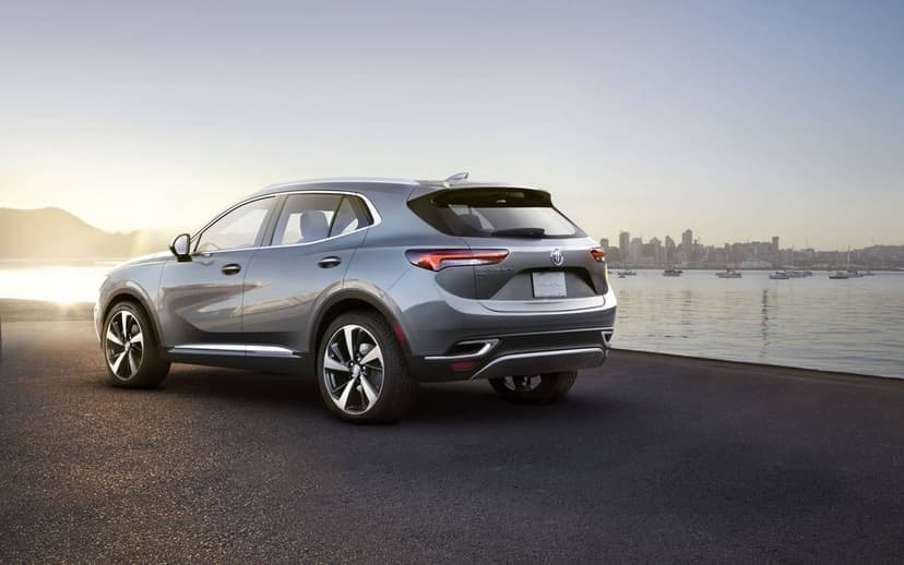 Silver Buick Envision SUV parked on a coastal road overlooking a harbor and city skyline at sunset.