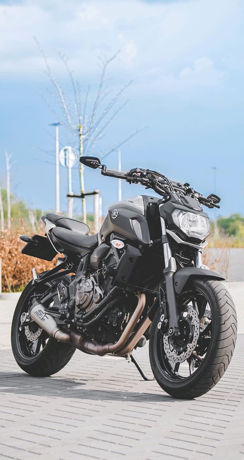 Yamaha MT-07 motorcycle in matte black parked on brick pavement under a blue sky with soft trees in background.