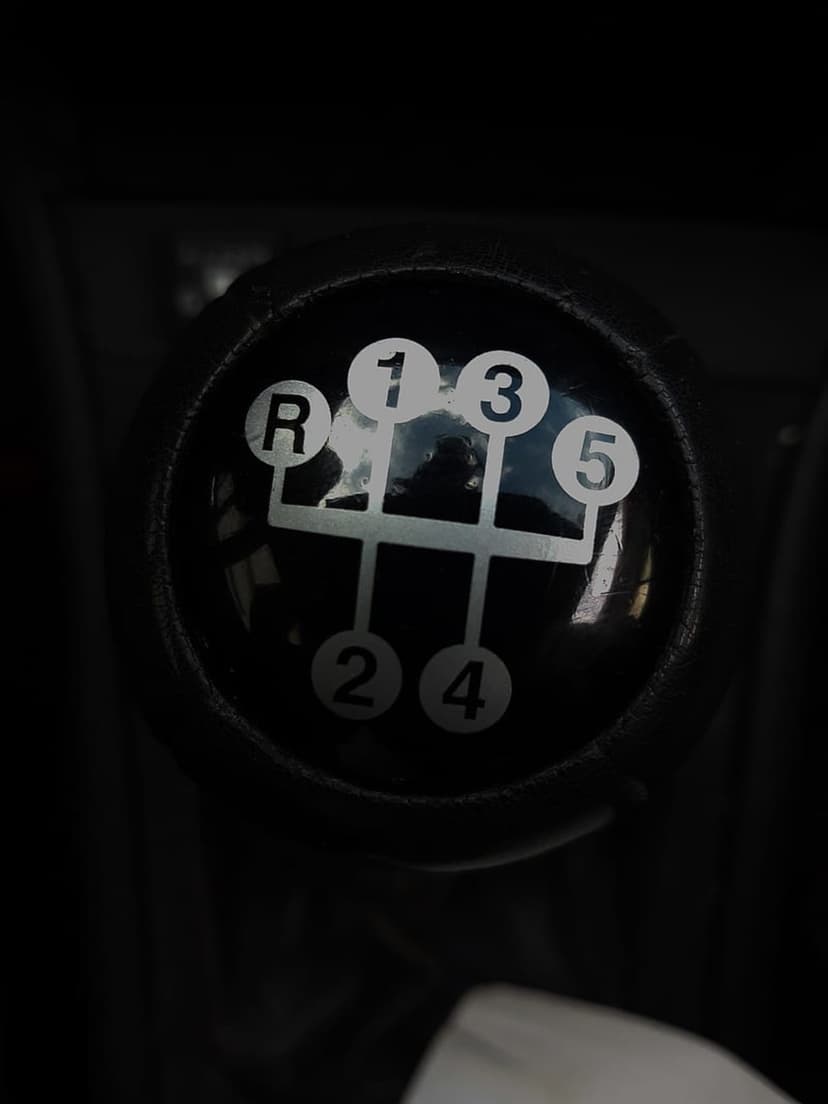 Black 5-speed manual gear shift knob with white H-pattern lettering reflects a dim car interior environment.