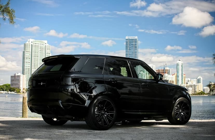 Black luxury SUV parked on a waterfront pier with a modern city skyline and blue sky in the background.