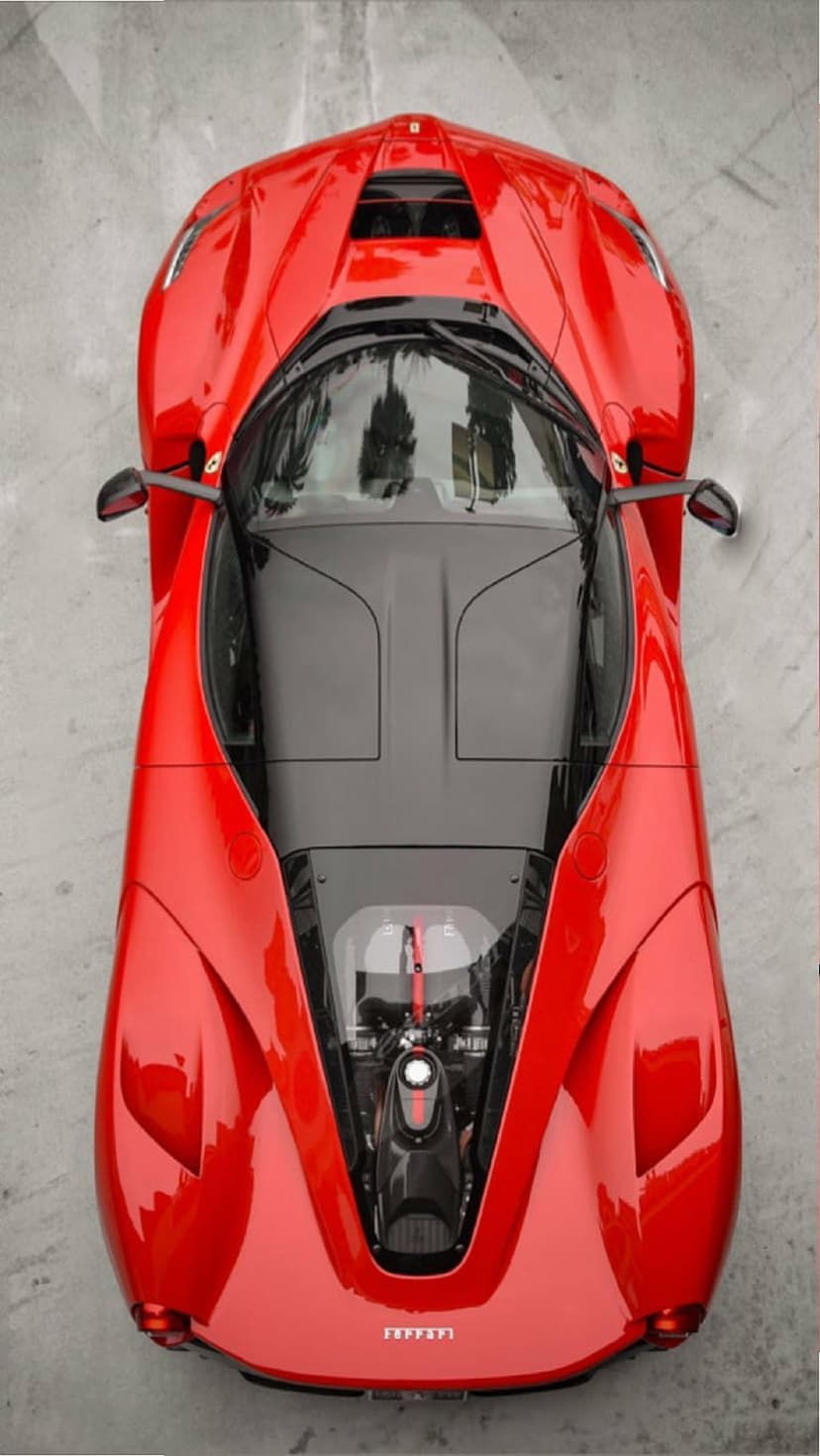 Red Ferrari hypercar viewed from above reveals its exposed engine and aerodynamic carbon fiber body contours.